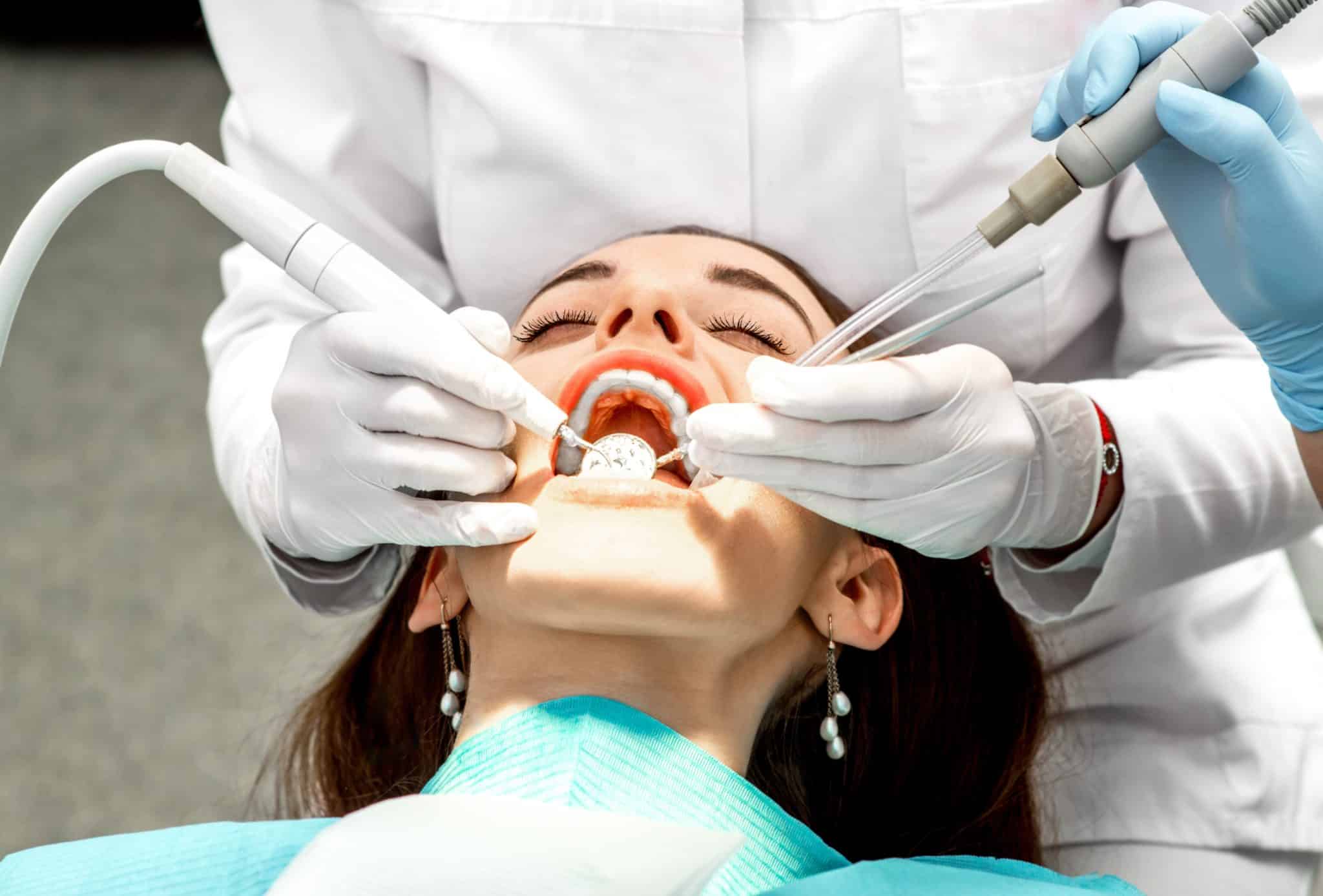 Gloved dental professionals using instruments to clean a person's teeth