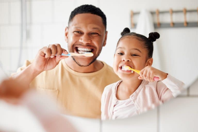 Happy father and daughter brushing their teeth together in a bathroom at home. Parent teaching his daughter to protect her teeth.